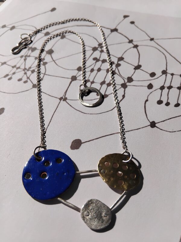 Mixed material necklace made from a Blue Enamelled Copper Circle, Hammered Brass Circle, and textured silver circle linked together to make and abstract constellation motif. hung on a silver chain. With Handmade S Hook Clasp.