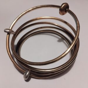 A brass bangle which spirals 5 rotations, It has 2 chunky silver beads and 1 chunky brass bead that orbit around the brass.